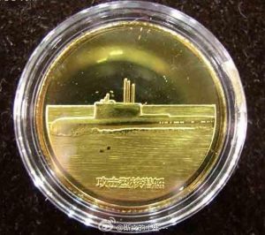 Une médaille commémorative en or montrant un sous-marin nucléaire d'attaque avec une plateforme rehaussée derrière le massif.